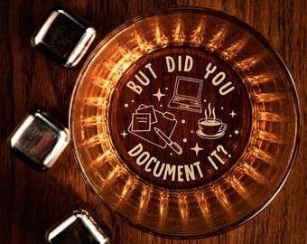 May include: A glass whiskey tumbler with a gold rim and a white inscription that reads "But did you document it?" The inscription is surrounded by small stars and icons of a laptop, a notepad, a pen, and a cup of coffee.