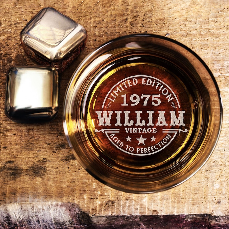 May include: A clear glass with a brown liquid inside. The glass has an engraved design that says "Limited Edition 1975 William Vintage Aged to Perfection".