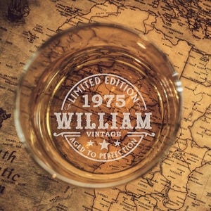 May include: A vintage-style glass with a label that reads "Limited Edition 1975 William Vintage Aged to Perfection". The glass is sitting on top of a vintage world map.