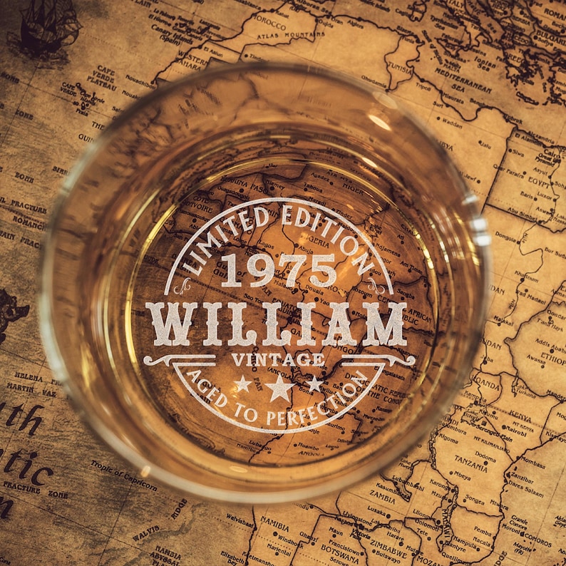 May include: A vintage-style glass with a label that reads "Limited Edition 1975 William Vintage Aged to Perfection". The glass is sitting on top of a vintage world map.