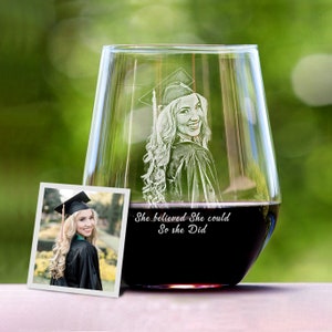 May include: A clear glass wine glass with an etched image of a person wearing a graduation cap and gown. The text "She believed She could So she Did" is etched on the glass.