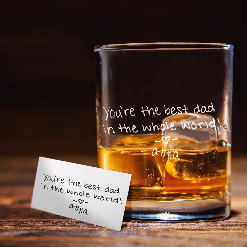 Puede incluir: Un vaso de vidrio transparente con un mensaje escrito a mano que dice "You're the best dad in the whole world! -♡- anna" en el lateral. El vaso est&aacute; lleno de l&iacute;quido &aacute;mbar y cubitos de hielo.