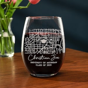 May include: A clear glass wine glass with a red wine inside. The glass is engraved with a map of the University of Michigan campus, a graduation cap, and the text "Christian Joe, University of Michigan, Class of 2025".