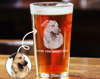 Puede incluir: Un vaso de pinta de vidrio transparente con cerveza marrón en su interior. El vaso tiene una imagen grabada de un perro y el texto "LOVE YOU, DADDY BOY".