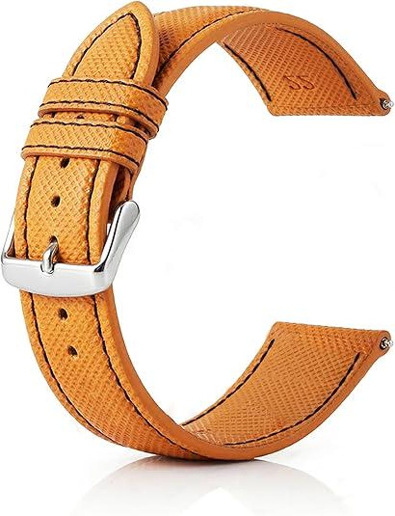 May include: A tan watch strap with a textured surface and black stitching. The strap features a silver buckle and is designed to attach to a watch face. The strap is made of a durable material.