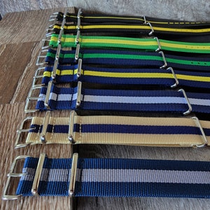 May include: A set of eight striped watch bands in various colors, including black, green, yellow, blue, and gray. The bands are made of nylon and have silver-toned buckles.
