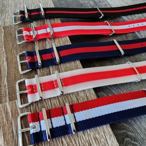 May include: Five different watch straps with red, white, and blue stripes. The straps are made of nylon and have silver buckles.
