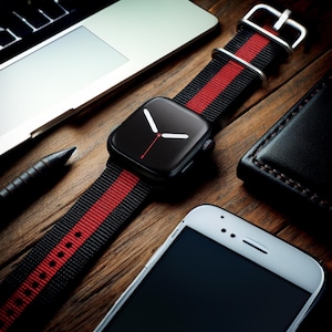 May include: A black Apple Watch with a red and black striped nylon band. The watch face is black with white hands and a red second hand.
