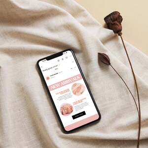 Op de afbeelding: Een mobiel telefoonscherm dat een e-mail weergeeft met de onderwerpregel "Echt een geweldige e-mail!" en de tekst "Nieuwe aankomsten" in een roze kader. De e-mail bevat twee afbeeldingen van kledingstukken met de tekst "Je nieuwe seizoensessentials zijn hier" en "Je nieuwe must-have is hier". De e-mail bevat ook een knop "Nu kopen".