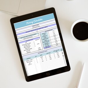 May include: A black tablet displays a pricing calculator spreadsheet with the title "Pricing Calculator." The spreadsheet includes sections for product name, quantity, and cost breakdown. A cup of coffee and a pen are next to the tablet.