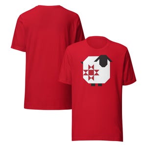 May include: Red t-shirt featuring a geometric sheep design. The sheep has a white body, black head and legs, and a red and white star pattern on its side. Another red t-shirt is visible in the background.