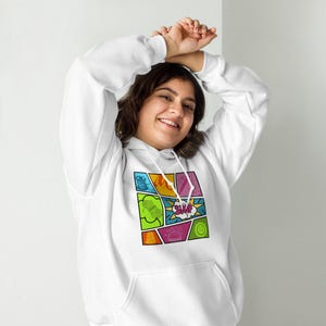 Op de afbeelding: Witte hoodie met een kleurrijke stripboekachtige afbeelding op de voorkant. De afbeelding bevat verschillende vormen en het woord "SWAP" in een tekstballon. De hoodie heeft een voorzak en een capuchon met trekkoord.