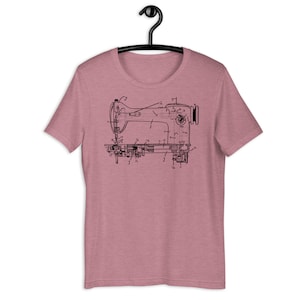 May include: A heather mauve short-sleeve t-shirt featuring a black line-art graphic of a vintage sewing machine patent diagram. The technical illustration includes various numbered labels and arrows pointing to specific mechanical components.