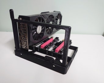 May include: A black metal frame with a graphics card mounted inside. The graphics card has a black and silver heatsink with a large fan. The frame has a series of pink connectors on the bottom.