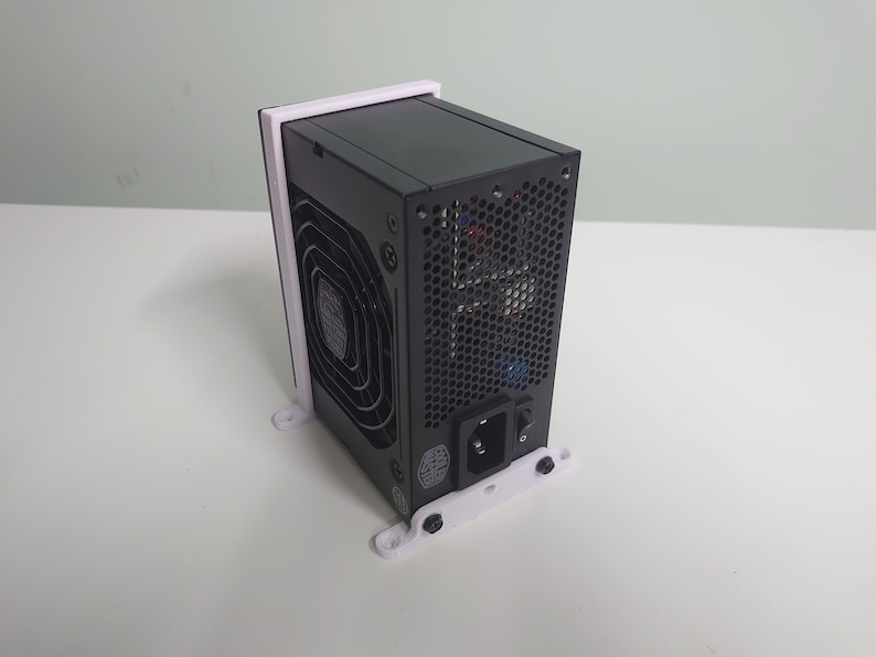 K&ouml;nnte beinhalten: Ein schwarzes Netzteil f&uuml;r Computer, das auf einer wei&szlig;en, 3D-gedruckten Halterung montiert ist. Das Netzteil hat einen L&uuml;fter und ein Netzkabel.