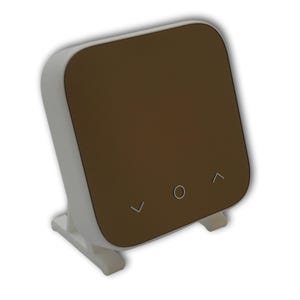 Puede incluir: Un termostato blanco y marrón con una pantalla digital y tres botones: arriba, abajo y un círculo. El termostato está en un soporte blanco.