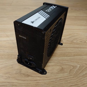 Może przedstawiać: Czarny zasilacz Corsair RM750i z czarną i białą etykietą z napisem "CORSAIR RM750i".