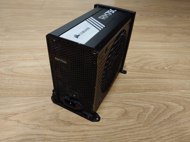 Może przedstawiać: Czarny zasilacz Corsair RM750i z czarną i białą etykietą z napisem "CORSAIR RM750i".