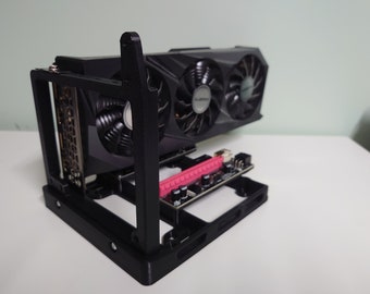 May include: A black 3D printed case for a small form factor computer. The case has a motherboard tray and a slot for a graphics card. The graphics card has two fans and is mounted vertically.