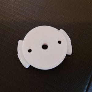 Op de afbeelding: Wit plastic 3D-geprint onderdeel met drie lipjes en een centraal gat.