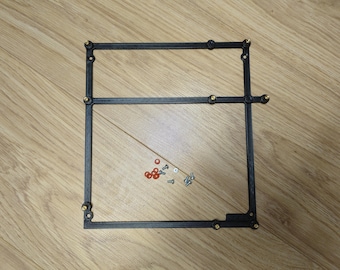 May include: A black rectangular frame with rounded corners and small gold-colored accents. Small red and silver hardware pieces are scattered inside the frame. The frame is resting on a wooden surface.