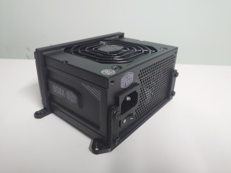 K&ouml;nnte beinhalten: Ein schwarzes Computer-Netzteil mit einem gro&szlig;en L&uuml;fter an der Seite. Das Ger&auml;t verf&uuml;gt &uuml;ber ein schwarzes Netzkabel und einen schwarzen Schalter. Das Ger&auml;t ist mit "Cooler Master V850" beschriftet.