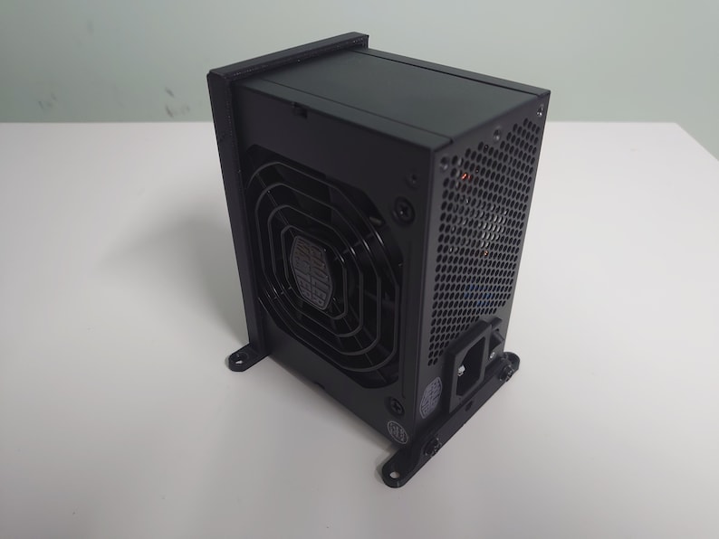 K&ouml;nnte beinhalten: Ein schwarzes Computer-Netzteil mit einem gro&szlig;en L&uuml;fter auf der R&uuml;ckseite. Das Ger&auml;t verf&uuml;gt &uuml;ber ein schwarzes Netzkabel und einen schwarzen Metallrahmen.