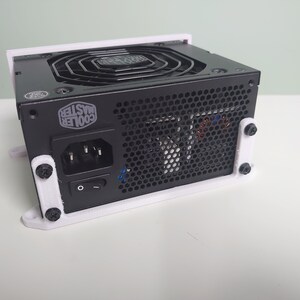 K&ouml;nnte beinhalten: Ein schwarzes Netzteil von Cooler Master mit einer wei&szlig;en Kunststoffhalterung. Das Netzteil hat einen L&uuml;fter, einen Netzschalter und einen Netzstecker.