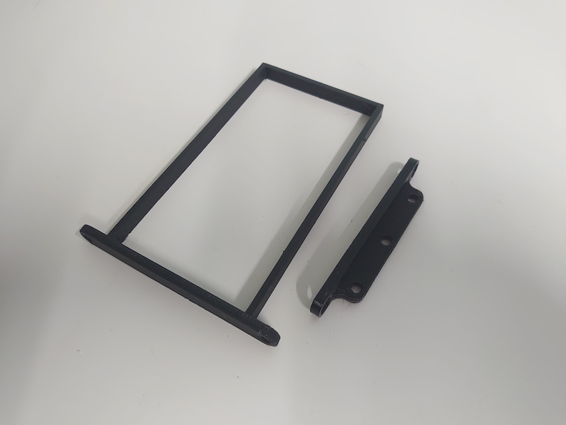 K&ouml;nnte beinhalten: Zwei schwarze, 3D-gedruckte Kunststoffteile f&uuml;r ein Projekt. Ein Teil ist ein rechteckiger Rahmen, der andere ist ein kleineres, flaches St&uuml;ck mit drei L&ouml;chern.