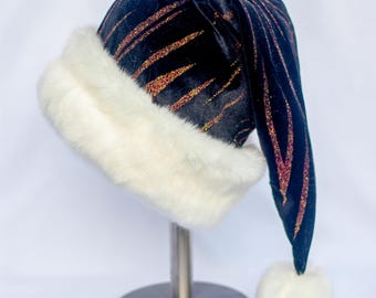 Könnte beinhalten: Ein schwarzer Weihnachtsmannhut mit weißem Kunstfellbesatz und einem passenden Bommel. Der Hut ist mit gold-orangenen Glitzerstreifen verziert. Der Hut wird auf einem silbernen Ständer präsentiert.