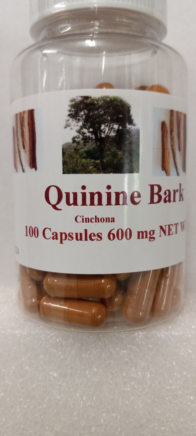 May include: A clear plastic bottle filled with brown capsules. The label reads "Quinine Bark Cinchona 100 Capsules 600 mg NET W".