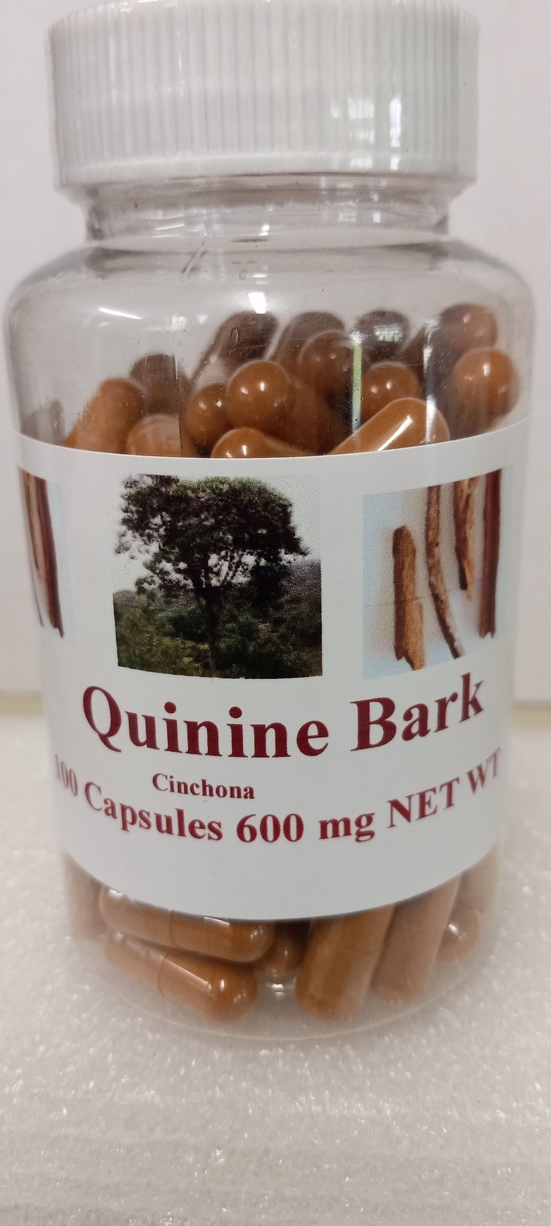 May include: A clear plastic bottle filled with brown capsules. The label reads "Quinine Bark Cinchona 100 Capsules 600 mg NET WT".