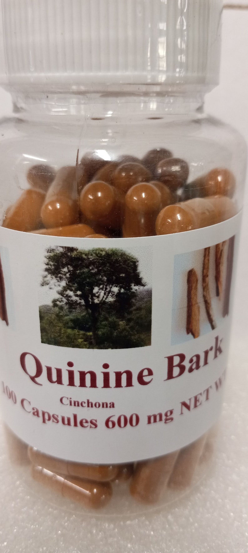 May include: A clear plastic bottle filled with brown capsules. The label reads "Quinine Bark Cinchona 100 Capsules 600 mg NET WT".
