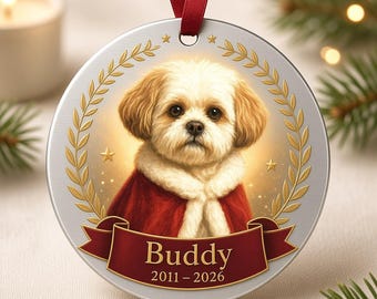 Puede incluir: Un adorno redondo de tono plateado con el retrato de un perro blanco y canela de pelaje esponjoso con una capa roja. El perro está enmarcado por hojas de laurel y estrellas doradas. Una cinta roja muestra el nombre Buddy y 2011-2026.