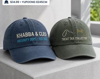 Puede incluir: Dos gorras de béisbol con texto bordado. La gorra azul presenta el texto KHABBA & CLEO SECURITY DEPT. EST. 2026. La gorra verde oliva muestra un icono de línea de perro y gato con el texto TREAT TAX COLLECTOR bordado debajo.