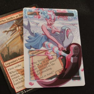 Può includere: Due carte di Magic: The Gathering. Una carta presenta Alesha, Who Smiles at Death, con testo. L'altra carta ha un'illustrazione stravagante di una persona che cavalca uno squalo, con il testo "DEAR EGGS".
