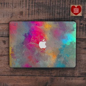 May include: A laptop computer with a colorful abstract design on the lid. The design features splashes of pink, blue, yellow, and green paint. The Apple logo is visible in the center of the lid.