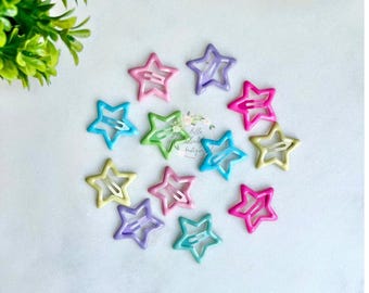 Puede incluir: Un conjunto de 10 pinzas para el pelo en forma de estrella en varios colores pastel, incluyendo rosa, azul, verde, amarillo y morado. Las pinzas están hechas de plástico y tienen un acabado brillante.