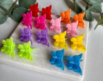 May include: A set of 12 colorful butterfly hair clips. The clips are made of plastic and come in a variety of colors, including pink, purple, blue, green, yellow, and orange.