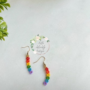 May include: Rainbow flower dangle earrings with gold hooks. The flowers are made of colourful beads and are arranged in a cascading pattern.