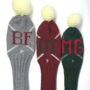 May include: Three knitted golf club head covers with pom-poms. The covers are gray, burgundy, and green. The gray cover has the letters "BF" embroidered on it. The burgundy cover has the letters "DIG" embroidered on it. The green cover has the letters "MEG" embroidered on it.