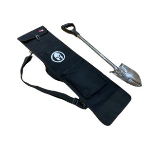 K&ouml;nnte beinhalten: Eine schwarze Stofftasche mit einem Schultergurt und einer Rei&szlig;verschlusstasche. Die Tasche hat ein wei&szlig;es Logo mit einem spartanischen Helm. Eine silberne Schaufel mit einem schwarzen Stiel liegt neben der Tasche.