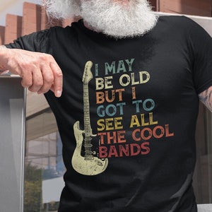 May include: A black t-shirt with a vintage-style graphic of a guitar and the text "I may be old but I got to see all the cool bands".