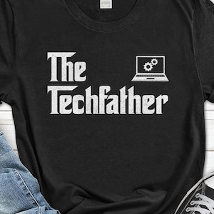 May include: Black t-shirt with the text "The Techfather" in a white, stylized font. A laptop graphic with gear icons is printed above the word "Techfather". The shirt is made of a soft material.