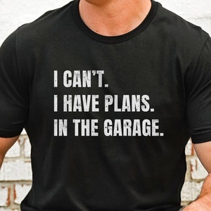 May include: Black crew neck t-shirt with white text that reads: "I CAN'T. I HAVE PLANS. IN THE GARAGE." The shirt is made of a soft material and is suitable for casual wear. The text is in a bold, sans-serif font.