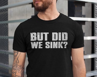 May include: Black t-shirt with the distressed white text "BUT DID WE SINK?". The shirt is short-sleeved and appears to be made of a soft material. The text is centered on the chest.