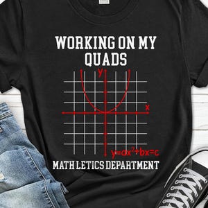 May include: Black t-shirt with the text "WORKING ON MY QUADS" above a red graph of a parabola. Below the graph is the equation "y=ax²+bx=c" and the words "MATH LETICS DEPARTMENT".