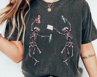 May include: Dark grey t-shirt with a graphic of two skeletons in lab coats, holding beakers and test tubes. The skeletons are dancing, with red, blue, and green liquids in the beakers. The shirt has a vintage, worn appearance.