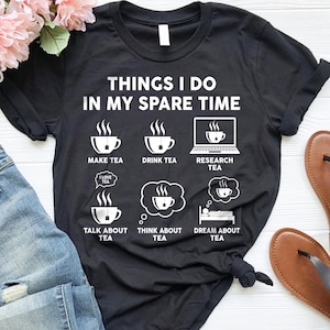 May include: Black t-shirt with white text that reads "Things I do in my spare time". The text is surrounded by illustrations of teacups and tea bags. The illustrations include "Make tea", "Drink tea", "Research tea", "Talk about tea", "Think about tea", and "Dream about tea".