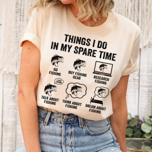 May include: A beige t-shirt with a black graphic that says "Things I do in my spare time" and lists activities related to fishing. The graphic includes illustrations of fish and fishing gear.